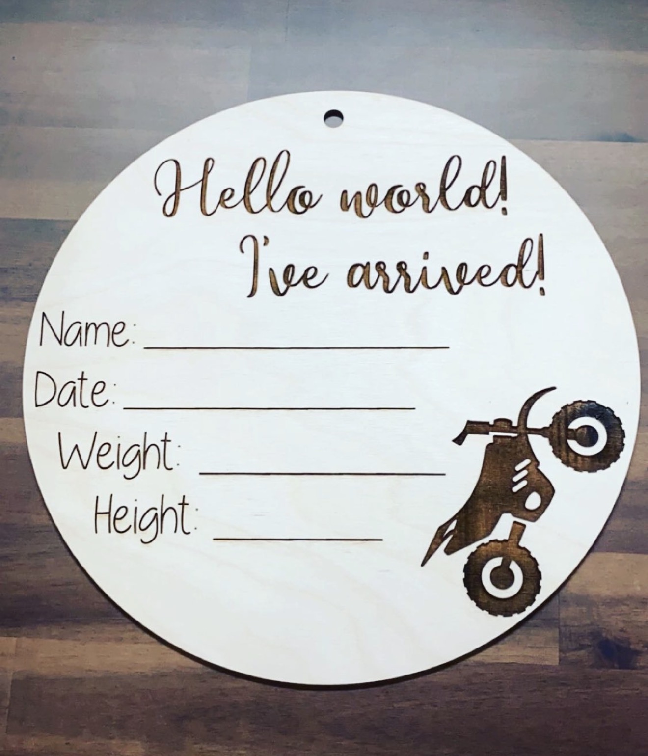 Round wooden 'Hello world, I've arrived!' baby announcement sign with a dirt bike illustration.